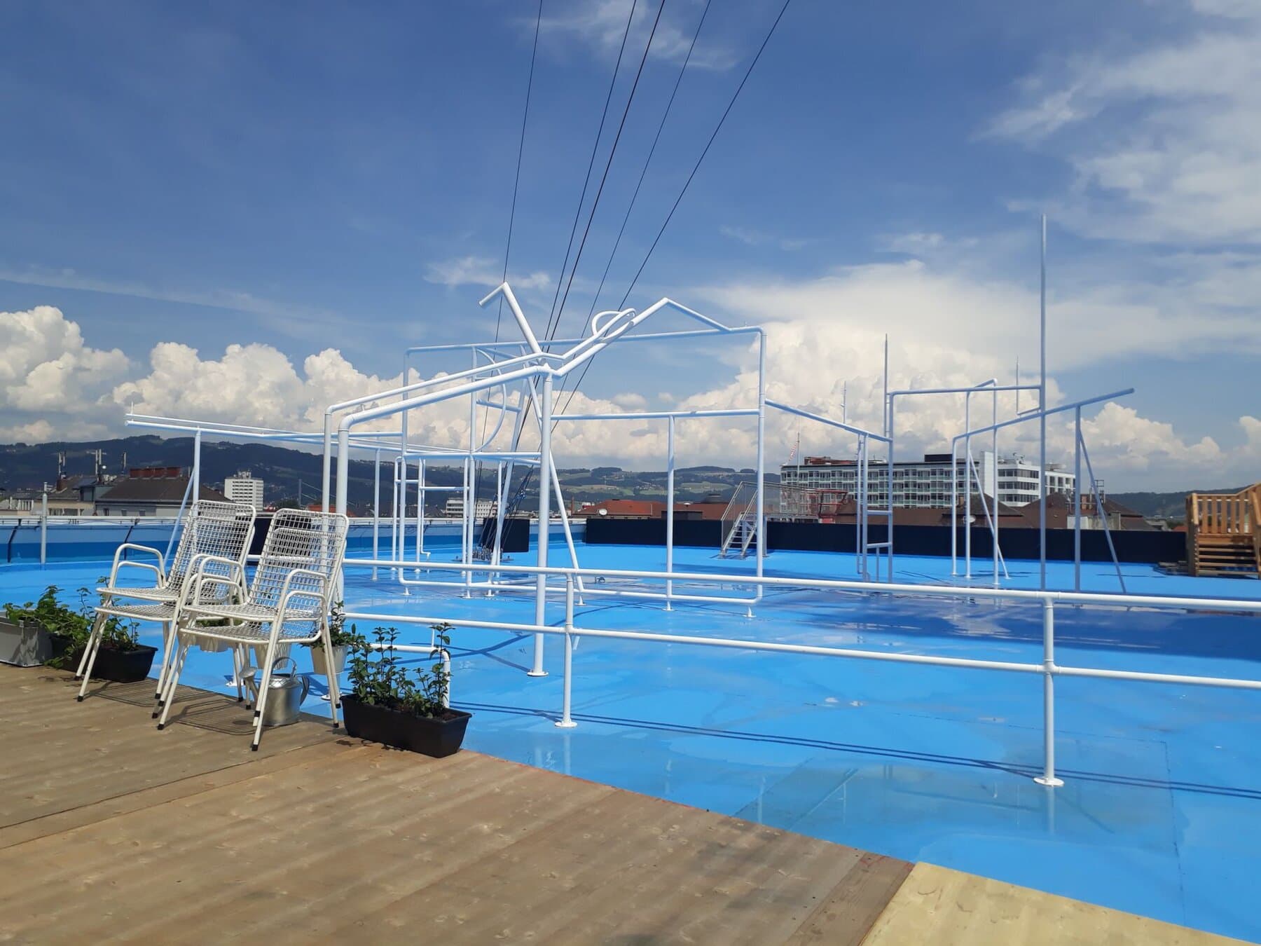 Blaue Dachterrasse mit filigranen weißen Stahlstrukturen und Holzdeck