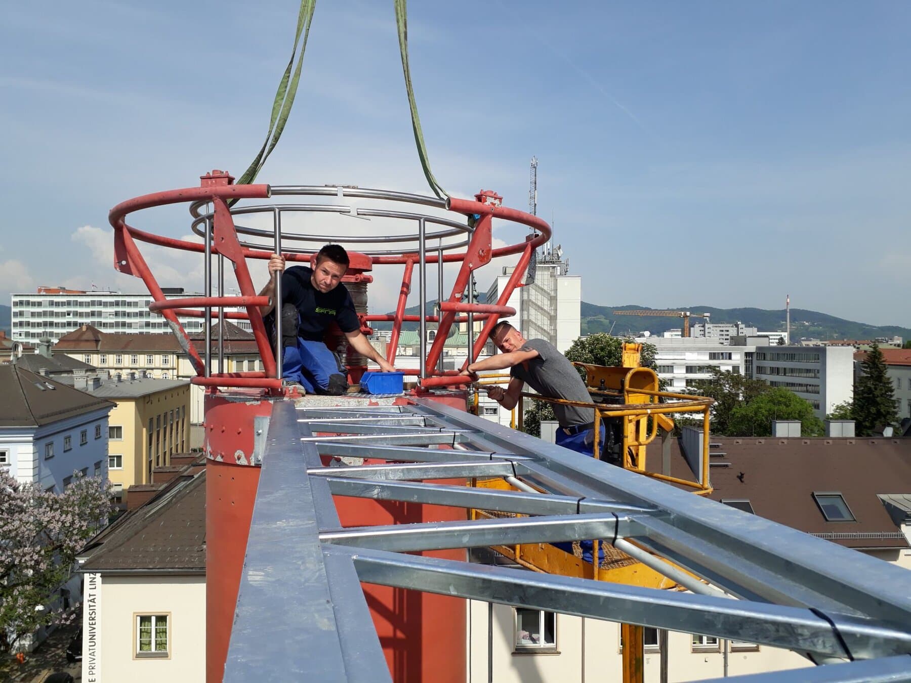 Roter Stahlring am Kran mit Monteuren über der Stadt